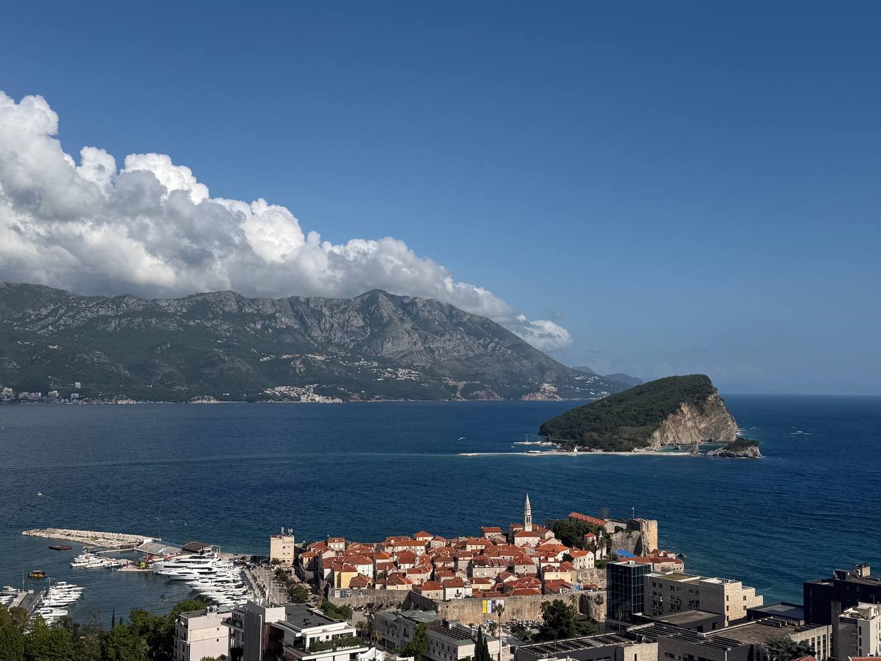 AI travel planner reviews from Budva, Montenegro, with the old town, Adriatic coast, Sveti Nikola island, and mountains in view.