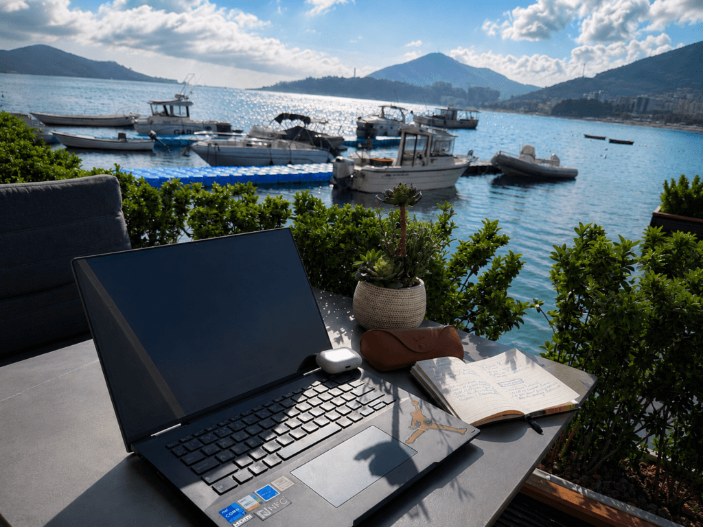 ChatGPT travel prompts planning setup with a laptop, open notebook, sunglasses case, and a seaside café view