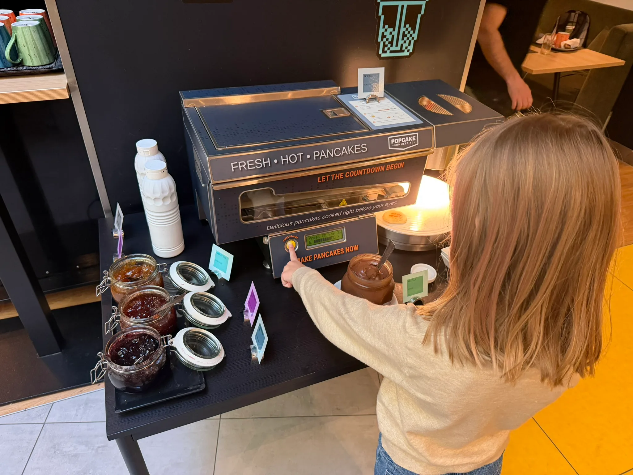Child pressing the Popcake automatic pancake machine at ibis Styles Budapest Center breakfast.